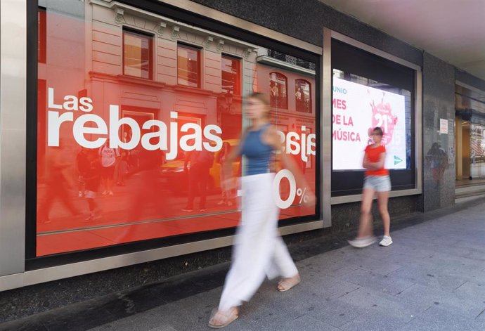 Archivo - Varias personas pasan al lado de un cartel de rebajas en un escaparate el día que comienzan las rebajas de verano 2023, a 22 de junio de 2023, en Madrid (España).