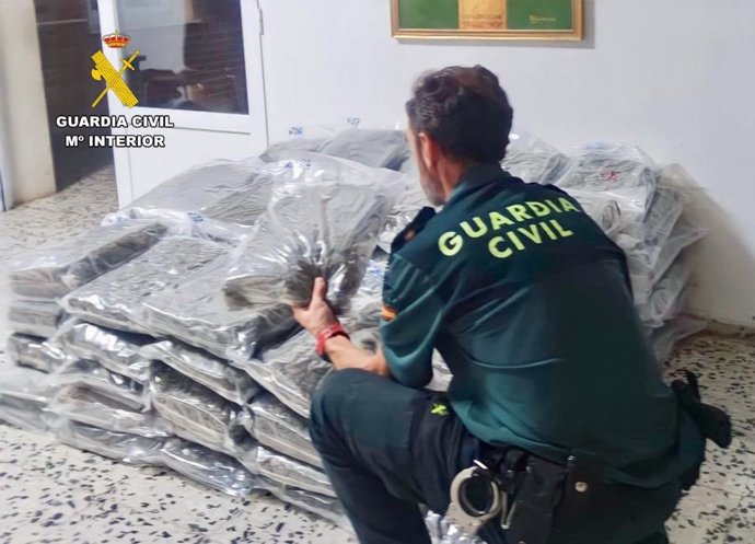Un guardia civil junto a los paquetes de cogollos de marihuana localizados en un vehículo cerca de Trujillo.