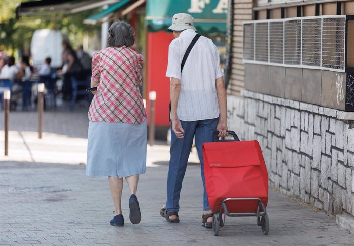 Una pareja de mayores caminan con un carro de la compra.