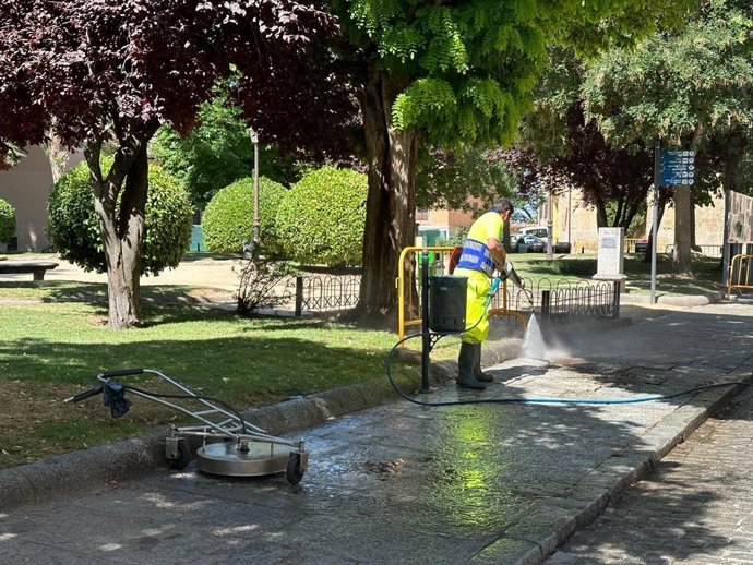 Un operario limpia con agua a presión una acera de Segovia.
