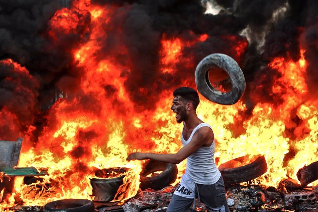 Archivo - 16 July 2019, Lebanon, Ain al-Hilweh: A Palestinian refugee runs past burning tires during a protest blocking the entrance of Ain al-Hilweh refugee camp against a decision by the Lebanese government to impose restrictions on the Palestinians' wo