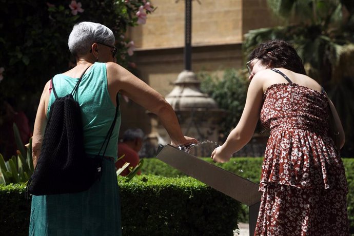 Dos mujeres  recoge agua de una fuente para combatir la ola de calor que estos días azota la capital a 19 de julio e 2023 en Málaga, Andalucía. 