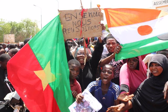 30 July 2023, Niger, Niamey: Demonstrators hold a flag of Burkina Faso (L) and Niger and a sign reading "Together we will make it" during a march in support of the coup plotters in the capital, centered . After the coup in Niger, thousands pledge their su