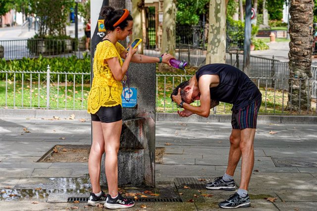 Una joven turista le hace una foto a un joven mientras le está refrescando la cabeza  el día en que la capital está en alerta naranja por el calor , a 19 de julio del 2023. La Agencia Estatal de Meteorología (Aemet) ha activado el aviso naranja en Sevilla