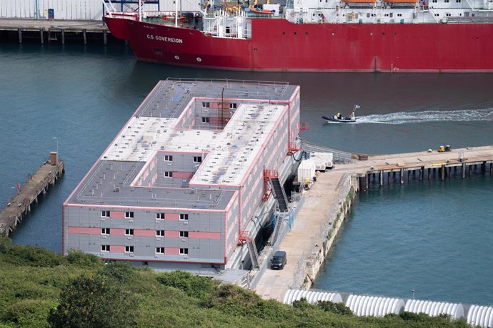 04 August 2023, United Kingdom, Portland: A boat passes the Bibby Stockholm accommodation barge at Portland Port in Dorset, which will house up to 500 people. The Home Office have said around 50 asylum seekers would board the Bibby Stockholm, with the n