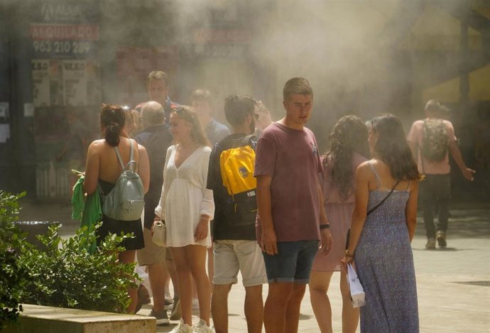 Varias personas se refugian del calor bajo unos vaporizadores de agua, este jueves en Valncia
