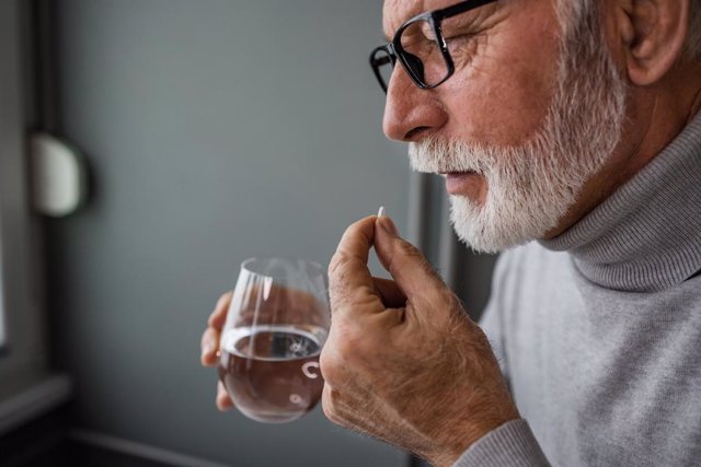 Hombre tomando un medicamento con un vaso de agua.