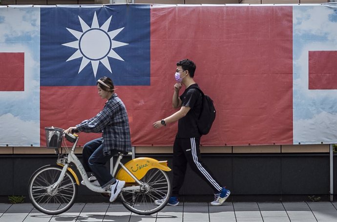 Archivo - June 21, 2023, Taipei, Taiwan, China: A woman riding a bicycle and a man on foot walk past a giant banner with the flag of the Republic of China in downtown in Taipei, Taiwan. During Secretary of State Blinken's visit two days ago, China reite