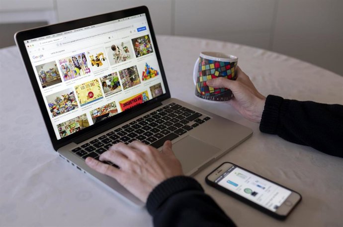 Archivo - Una persona compra con su teléfono móvil y ordenador