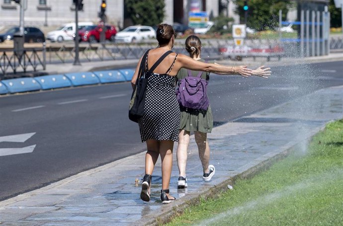 Dos mujeres se mojan con unos chorros de regadío, a 21 de agosto de 2023, en Madrid (España).  