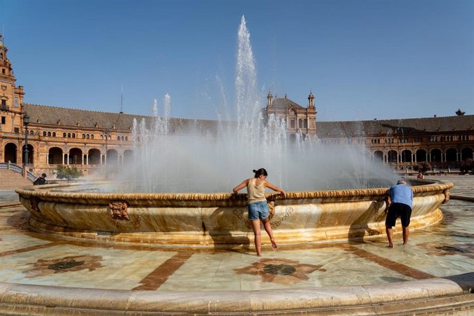 Turistas se refrescan en la fuente de la Plaza de España,  en Sevilla (Andalucía, España).