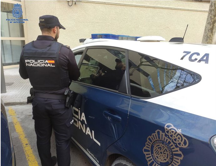 Agente de la Policía Nacional de espaldas, junto a un coche patrulla.