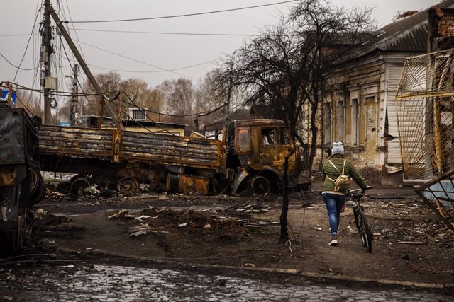 Archivo - April 2, 2022, Trostyanets, Sumy, Ukraine: A woman walks her bike around destroyed Russian vehicles at Trostyanets, Ukraine on April 2, 2022. Russian troops held the city but have since been pushed back by Ukrainian forces.,Image: 676669337, Lic