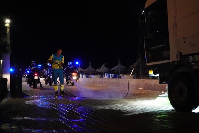 Un profesional de Emaya limpia con agua una calle de Playa de Palma acompañado de Policía.