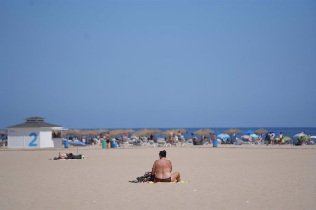 Una persona sentada en una toalla en la playa durante la cuarta ola de calor del verano