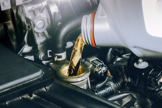 Un mecánico rellena de aceite el motor de un vehículos.
