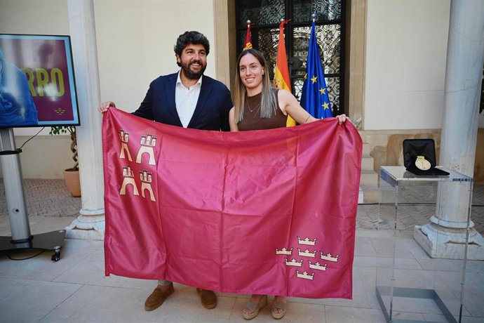 El jefe del Ejecutivo autonómico en funciones, Fernando López Miras, y la campeona del Mundial de Fútbol Femenino, la yeclana Eva Navarro, posan con una bandera de la Región de Murcia