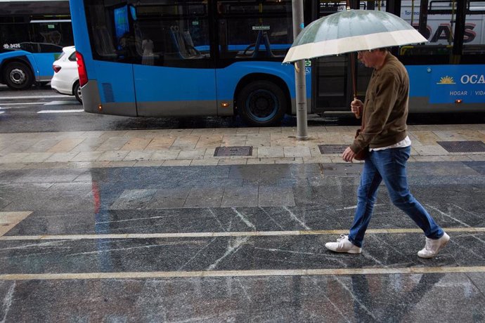 Archivo - Un hombre con paraguas camina bajo la lluvia