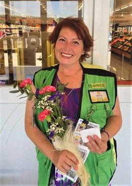 Imagen:  M Teresa Fernández, vendedora ONCE, hoy en su puesto de trabajo con un ramo de flores regalado por uno de sus clientes y una nota de felicitación.