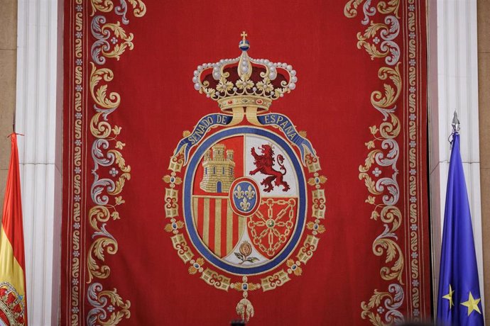 Escudo en el hemiciclo del Senado que se basa en las normas existentes sobre el Escudo de España, en el que se inspiran los cuarteles, y en el Escudo de armas de la monarquía española, en el que se inspiran la forma y los adornos, a 17 de agosto de 2023