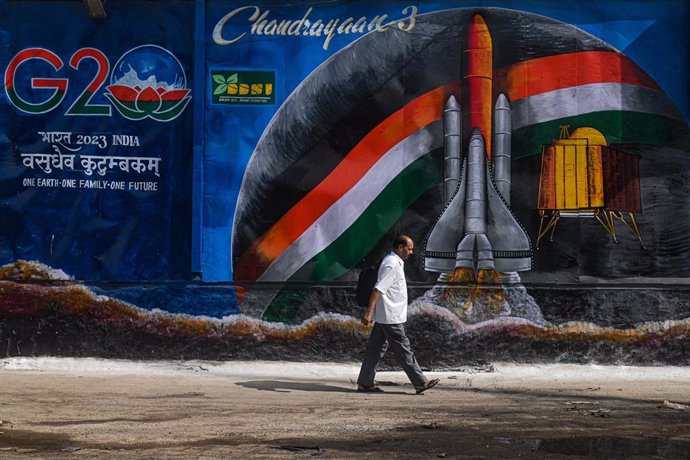 Un hombre camina por al lado de un mural rodeado de un montón de basura al lado del logo de la próxima reunión del G20 en La India. 6 de septiembre de 2023, Nueva Delhi, India.