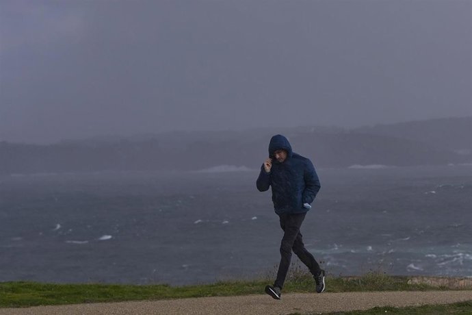 Archivo - Un hombre se protege del viento y la lluvia en la zona de la Torre de Hércules en A Coruña