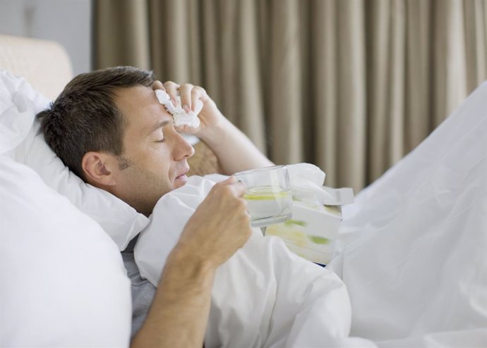 Archivo - Hombre enfermo en la cama con una bebida caliente.