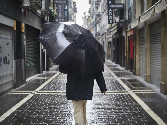 Archivo - Un hombre camina protegiéndose con un paraguas por la lluvia.