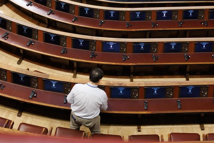 Un hombre prepara los asientos del hemiciclo antes de iniciar una sesión plenaria en la se aprueba el uso de las lenguas cooficiales en el Congreso de los Diputado.