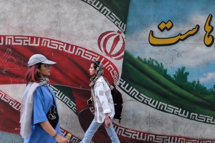 Dos mujeres iraníes caminan por la capital (Teherán) delante de un mural con la bandera del país