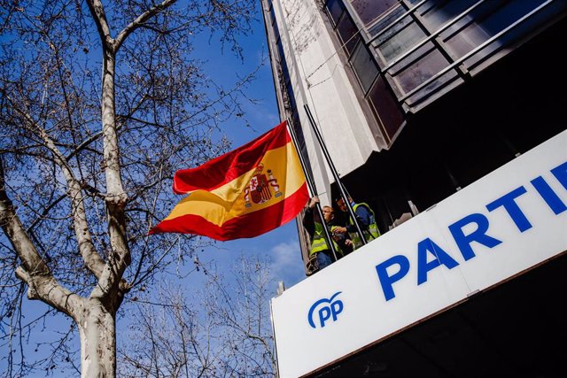 Archivo - Dos trabajadores colocan una bandera de España en la sede del PP de la calle Génova, a 13 de marzo de 2023, en Madrid (España).