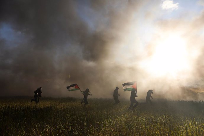 Archivo - 22 February 2023, Palestinian Territories, Gaza: Palestinians hold the Palestinian flags in front of burned tires during a protest on the eastern borders of the Gaza Strip against the Israeli army. At least 10 Palestinians were killed in an Is