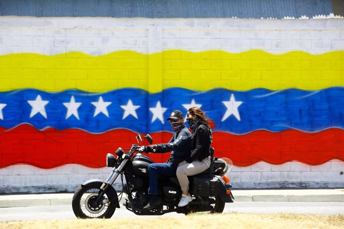Archivo - March 21, 2020, Valencia, Carabobo, Venezuela: March 21, 2020. A couple of motorized people walk in front of a grafitty with the flag of Venezuela, the venezuelans have accepted the call to stay at home, leaving only in emergencies, to look for 