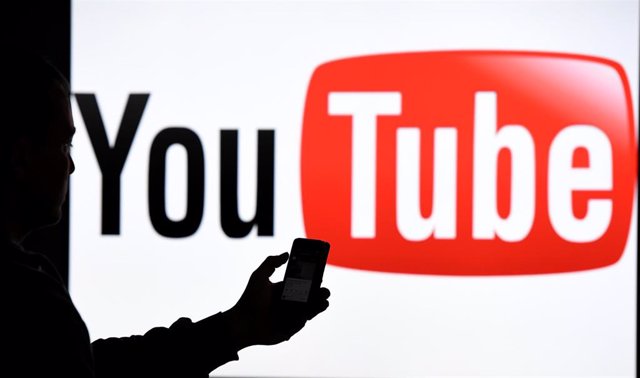 Archivo - Una persona con un móvil junto a un logo de YouTube
