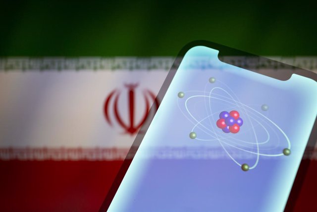 Archivo - August 9, 2022, Asuncion, Paraguay: Visual representation of an atom, electrons in orbitals, and neutrons and protons in the nucleus, displayed on a smartphone backdropped by cropped flag of Iran.