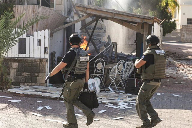 07 October 2023, Israel, Ashkelon: Israeli officers walk next to a destroyed house during a rocket attack from Gaza. Palestinian militants in Gaza unexpectedly fired dozens of rockets at Israeli targets early on Saturday, the Israeli army said.