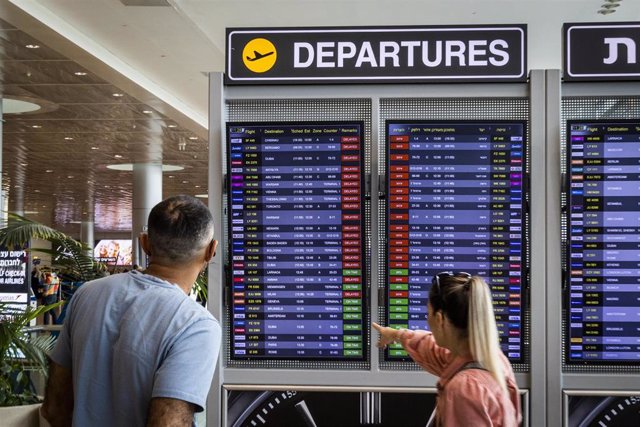 Archivo - Varias personas permanecen de pie ante el tablero de salida del aeropuerto Ben Gurion.