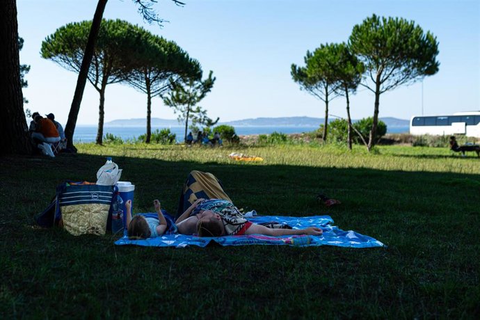 Un hombre y un niño descansan a la sombra de un árbol, a 30 de septiembre de 2023, en Sanxenxo, Pontevedra, Galicia.