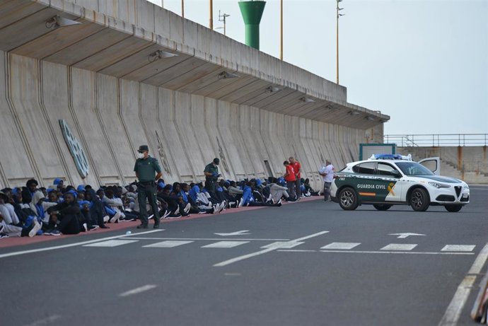 Un vehículo y agentes de la Guardia Civil al lado de los migrantes que esperan a ser trasladados, en el muelle de la Restinga, a 11 de septiembre de 2023, en El Hierro, Canarias (España). En la mañana de hoy se ha procedido al traslado de más de 400 inm