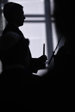 Archivo - Una persona sujeta una vela durante una ceremonia para conmemorar el Holocausto, en Madrid el pasado enero