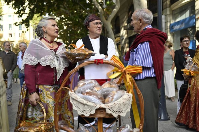 Un grupo de tres personas con los trajes típicos y una cesta de alimentos durante la ofrenda de frutos a la Virgen del Pilar.