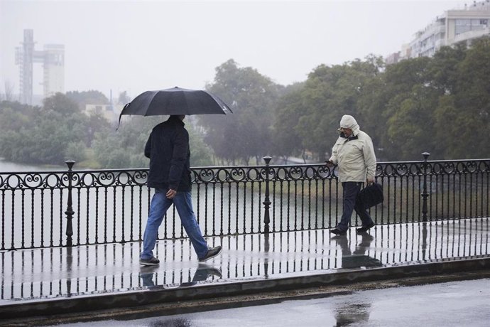 Archivo - Dos personas cruzan el puente de Isabel II durante la lluvia caída en la capital andaluza, a 11 de marzo de 2022 en Sevilla (Andalucía, España).