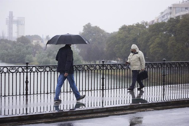 Archivo - Dos personas cruzan el puente de Isabel II durante la lluvia caída en la capital andaluza, a 11 de marzo de 2022 en Sevilla (Andalucía, España)