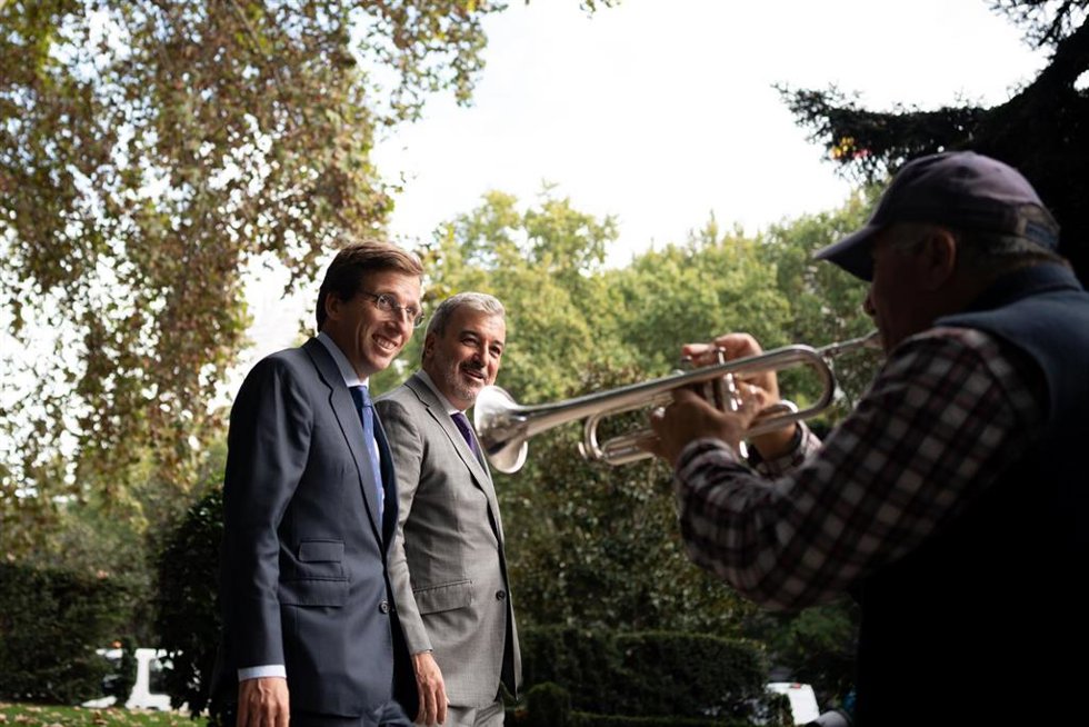 Un hombre toca la trompeta en la calle mientras que el alcalde de Madrid, José Luis Martínez-Almeida (i) y el alcalde de Barcelona, Jaume Collboni (d), dan un paseo por el Paseo del Prado, tras un encuentro institucional, en el Palacio de Cibeles,