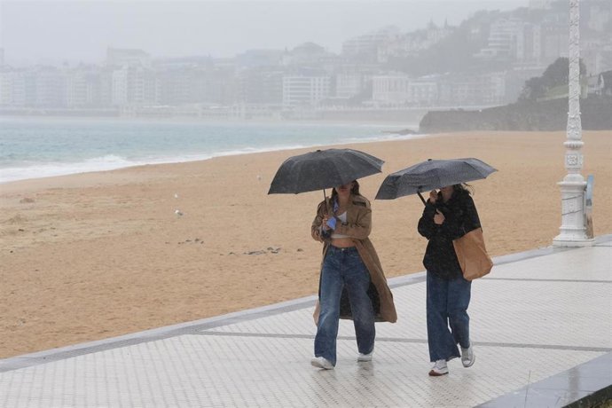 Dos mujeres caminan con paraguas en la playa de Ondarreta, a 14 de octubre de 2023, en San Sebastián, Guipúzcoa, País Vasco (España). 