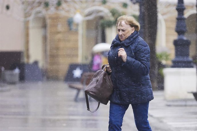 Archivo - Una señora se acelera para evitar el viento y la lluvia