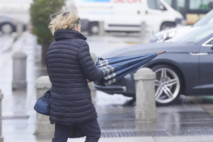 Archivo - Una señora cierra el paraguas tras el fuerte viento en Cádiz. ARCHIVO