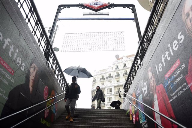 Archivo - Personas entran al metro con paraguas y mojadas por la lluvia