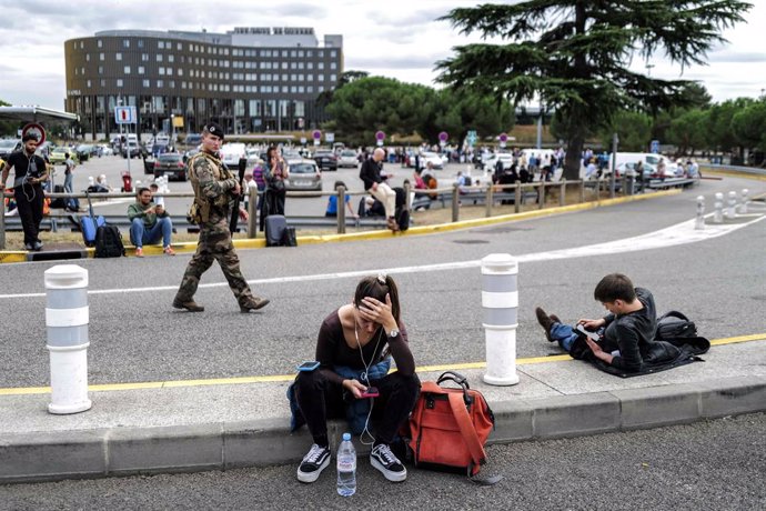 18 October 2023, France, Blagnac: Travelers wait while a French soldier patrols outside Toulouse-Blagnac airport. Six airports across France were evacuated because of bomb threats. Bomb threats in France led to the evacuation of airports in Lille, Lyon 
