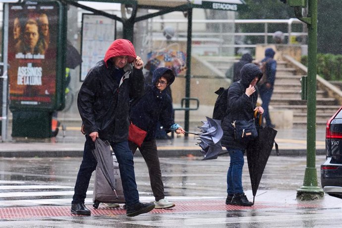 Varias personas tratan de cubrirse de la lluvia y el viento